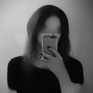 A grayscale picture of a long-haired person wearing over-the-ear headphones, holding a mobile phone, parially covering their face (taking a selfie). Parts above the nose and below the shoulders heavily blurred.